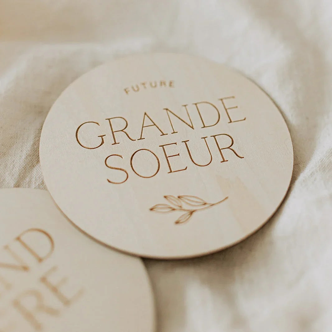 Plaque ronde en bois clair gravée « Future Grande Soeur » avec motif feuille sur tissu beige