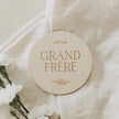 Plaque ronde en bois naturel avec inscription 'Futur Grand Frère' sur tissu beige clair avec fleurs blanches