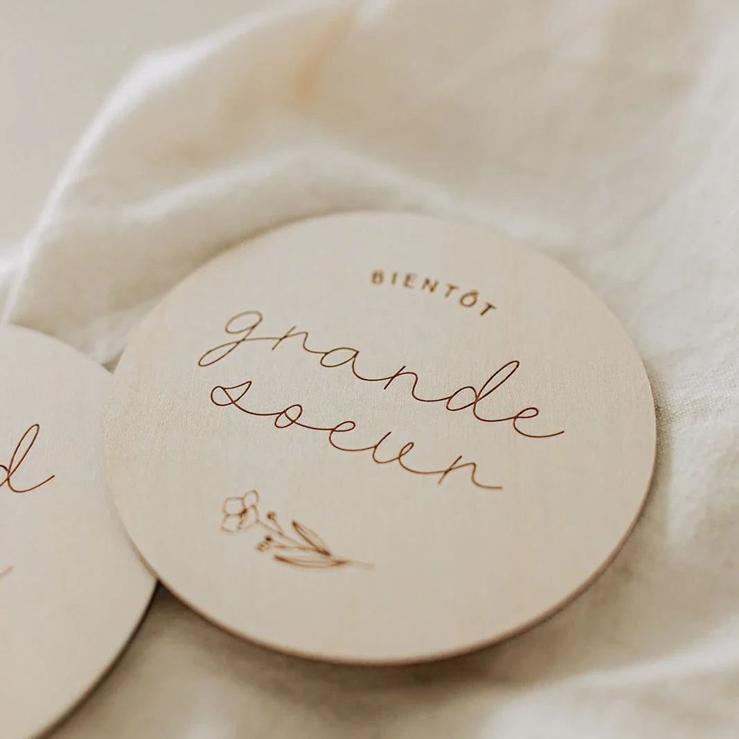 Disque en bois gravé "Bientôt grande soeur" sur tissu beige, décoration douce et naturelle