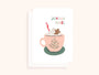 Carte de Noël illustrée d'une tasse rose avec chocolat chaud, chantilly, bonhomme en pain d'épice et texte Joyeux Noël