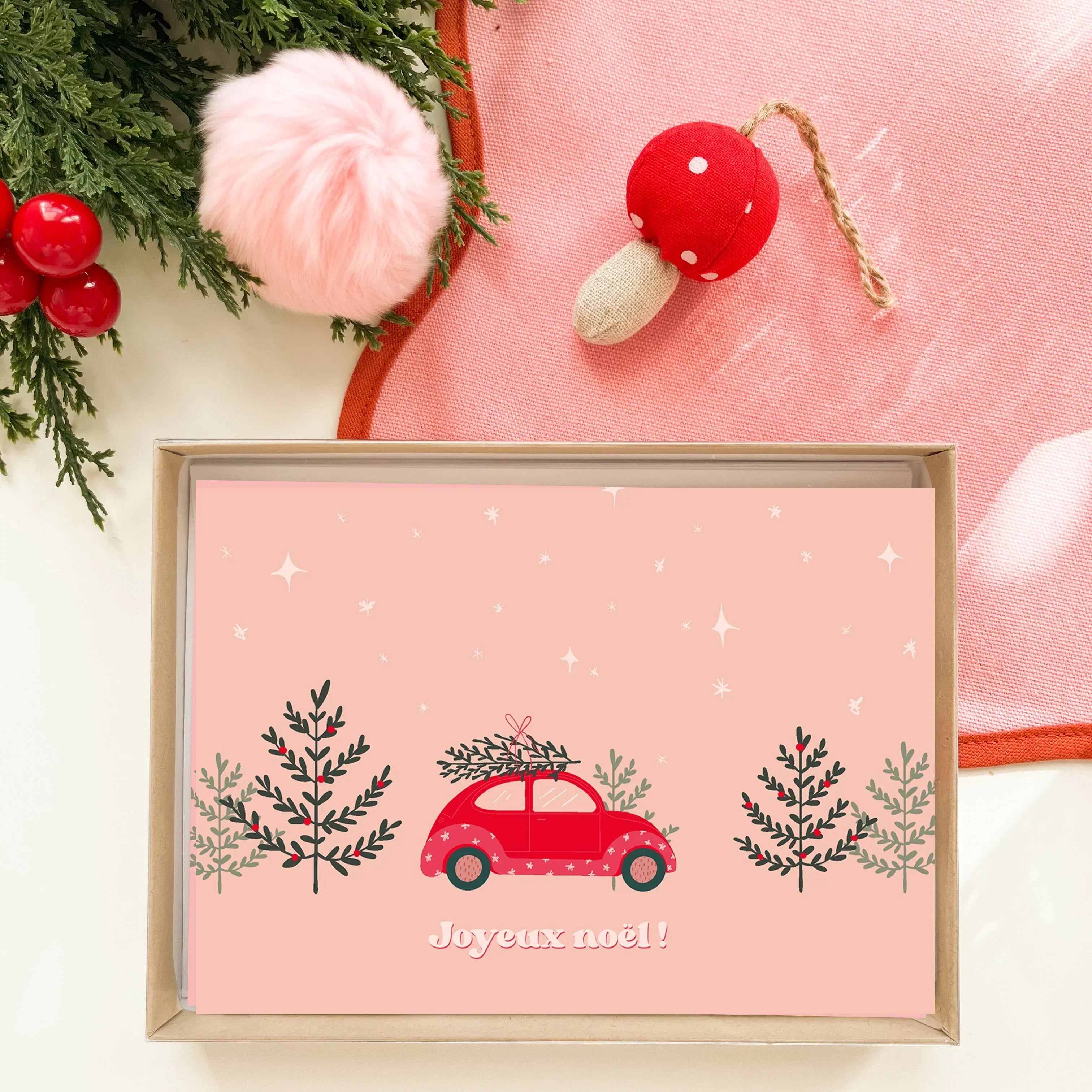 Carte de Noël rouge illustrée avec voiture transportant un sapin, entourée de décorations et cerises rouges