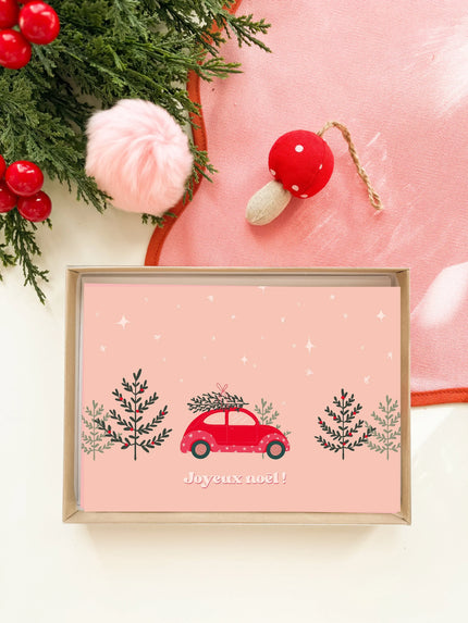 Carte de Noël rouge illustrée avec voiture transportant un sapin, entourée de décorations et cerises rouges
