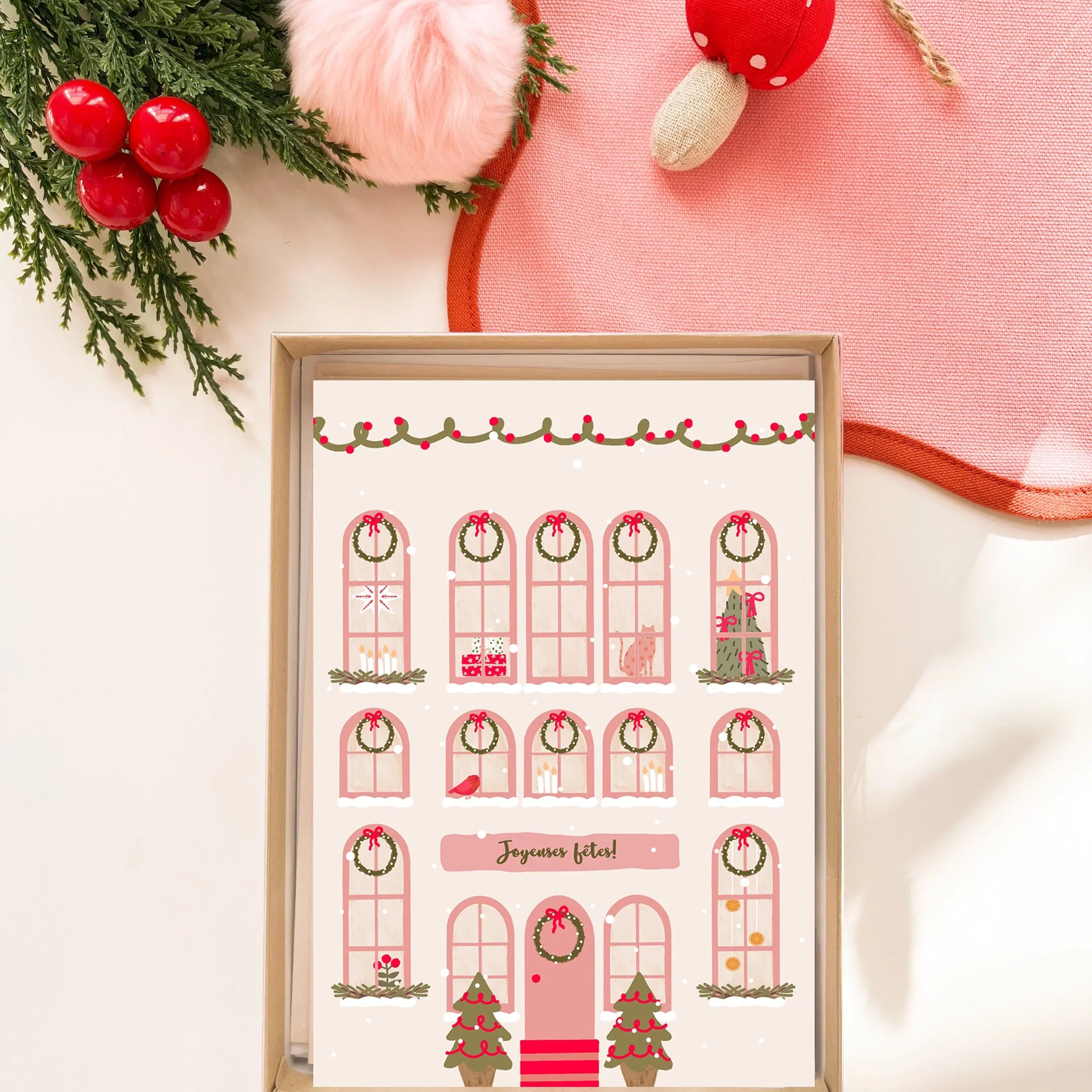 Carte de vœux festive illustrée avec façade de maison décorée de guirlandes, sapins, bougies et message Joyeuses fêtes