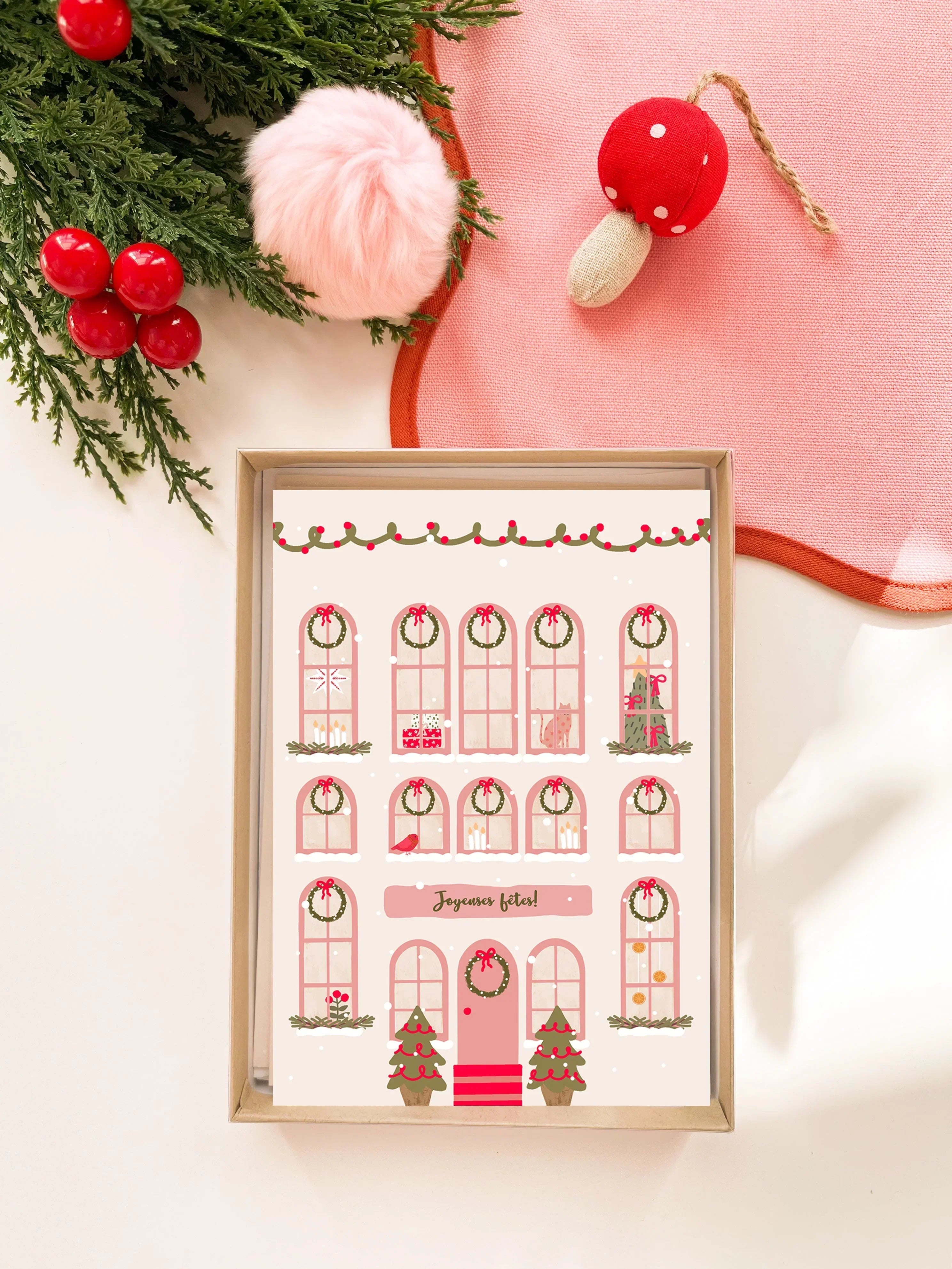 Carte de vœux festive illustrée avec façade de maison décorée de guirlandes, sapins, bougies et message Joyeuses fêtes