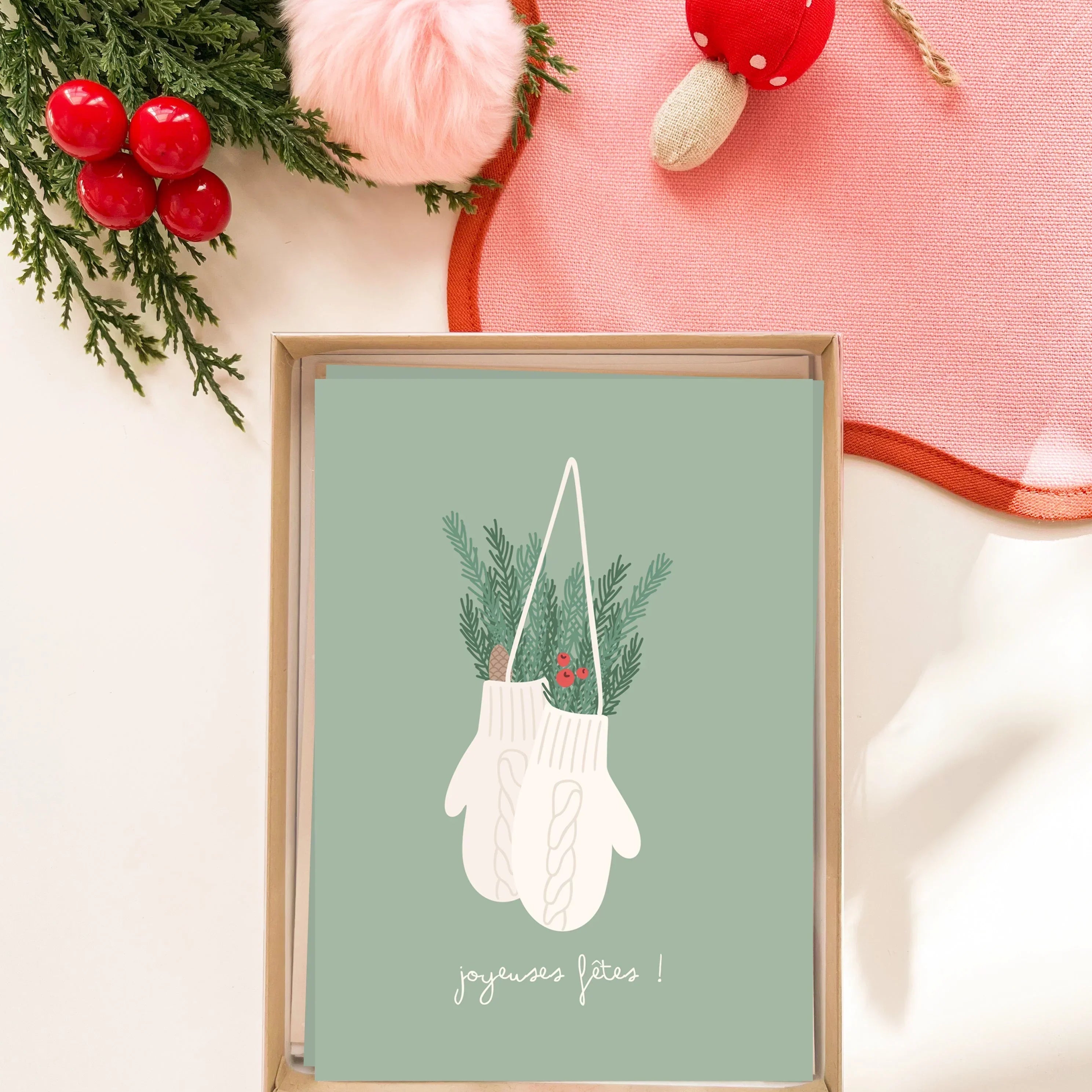 Carte de vœux illustrée avec mitaines blanches, feuillage de sapin et texte joyeuses fêtes