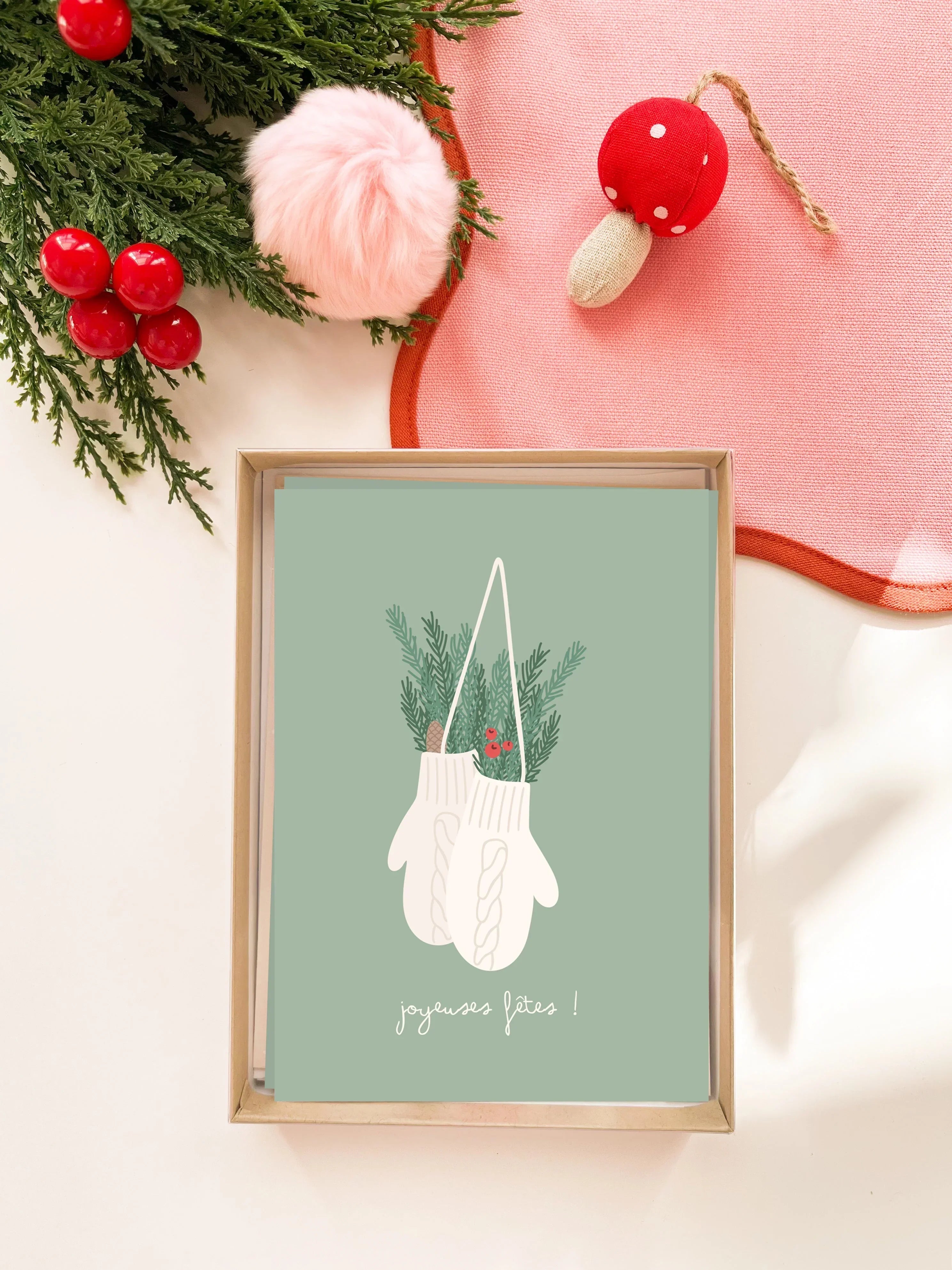 Carte de vœux illustrée avec mitaines blanches, feuillage de sapin et texte joyeuses fêtes