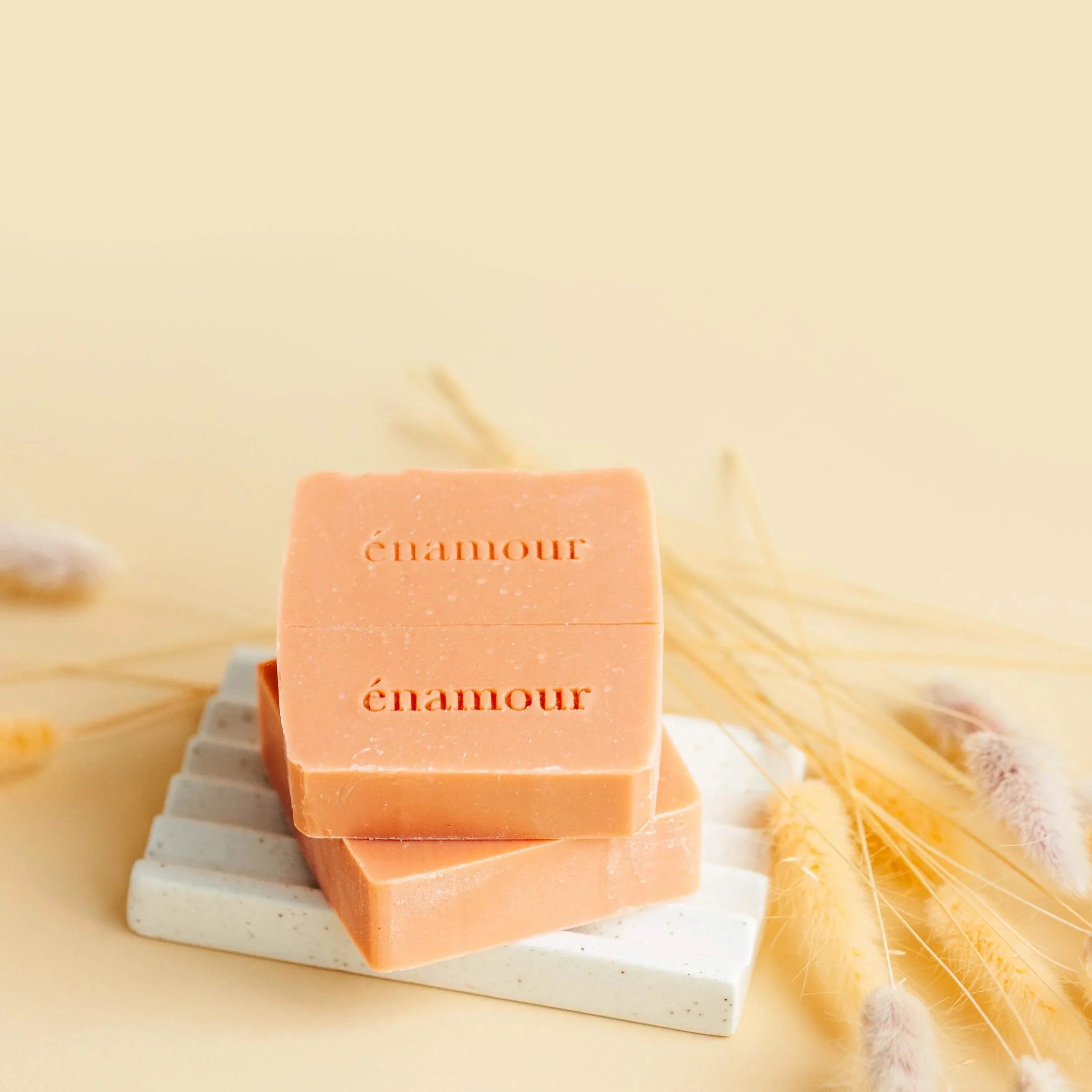 Savon orange marqué énamour sur porte-savon blanc, décoré de graminées séchées jaunes et beiges