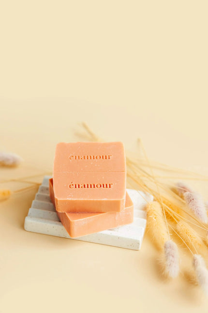 Savon orange marqué énamour sur porte-savon blanc, décoré de graminées séchées jaunes et beiges