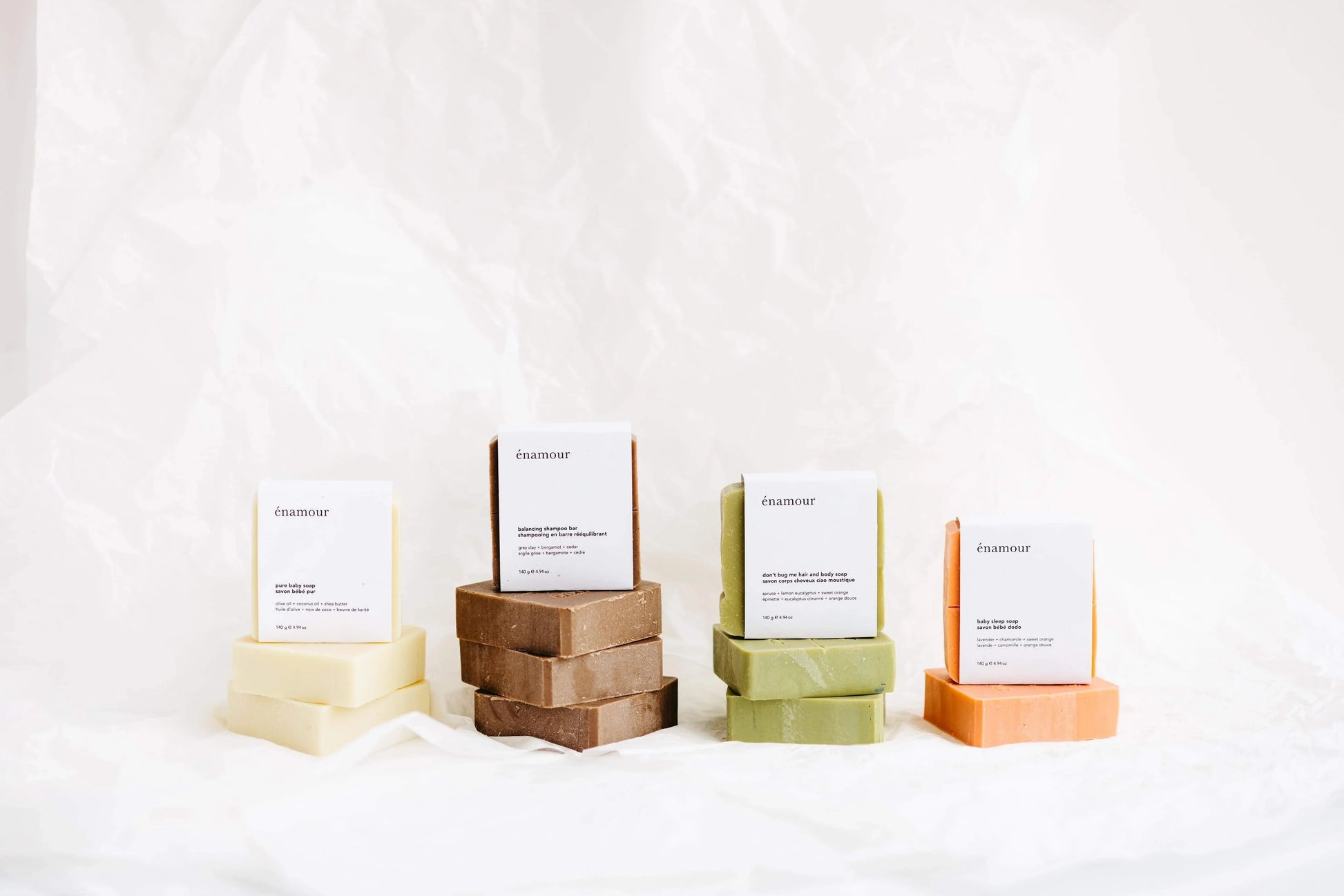 Quatre piles de savons naturels énamour aux couleurs crème, marron, vert et orange sur fond blanc