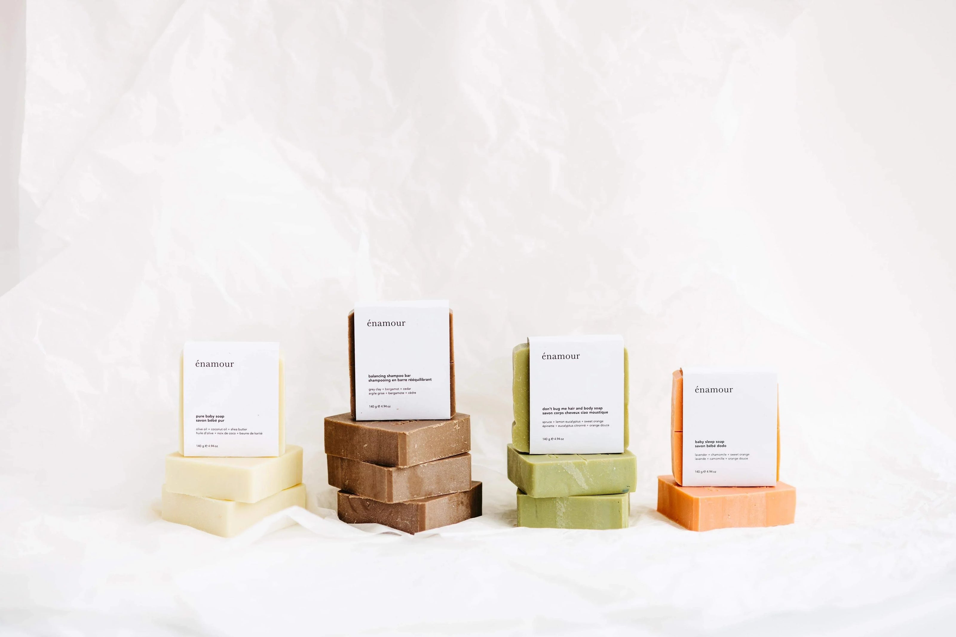 Quatre piles de savons naturels énamour aux couleurs crème, marron, vert et orange sur fond blanc