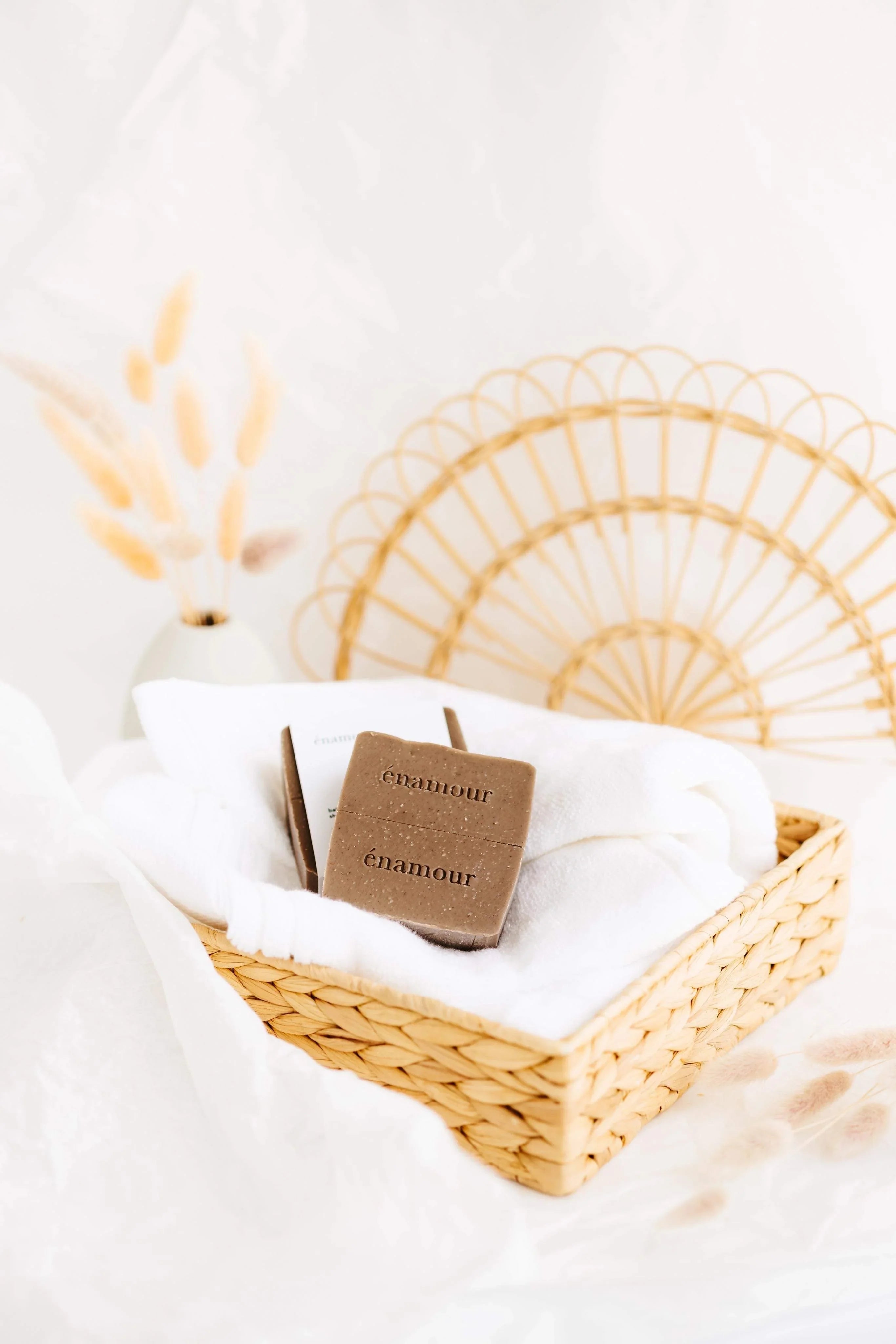 Panier en osier avec serviette blanche et deux savons marron marqués énamour sur fond blanc