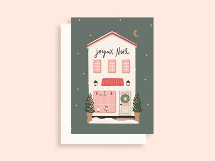Carte de Noël illustrée avec maison décorée, sapins, couronne et texte joyeux Noël