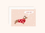 Carte de Noël illustrée avec chien portant un pull rouge à motifs floraux et cache-oreilles, fond beige avec flocons