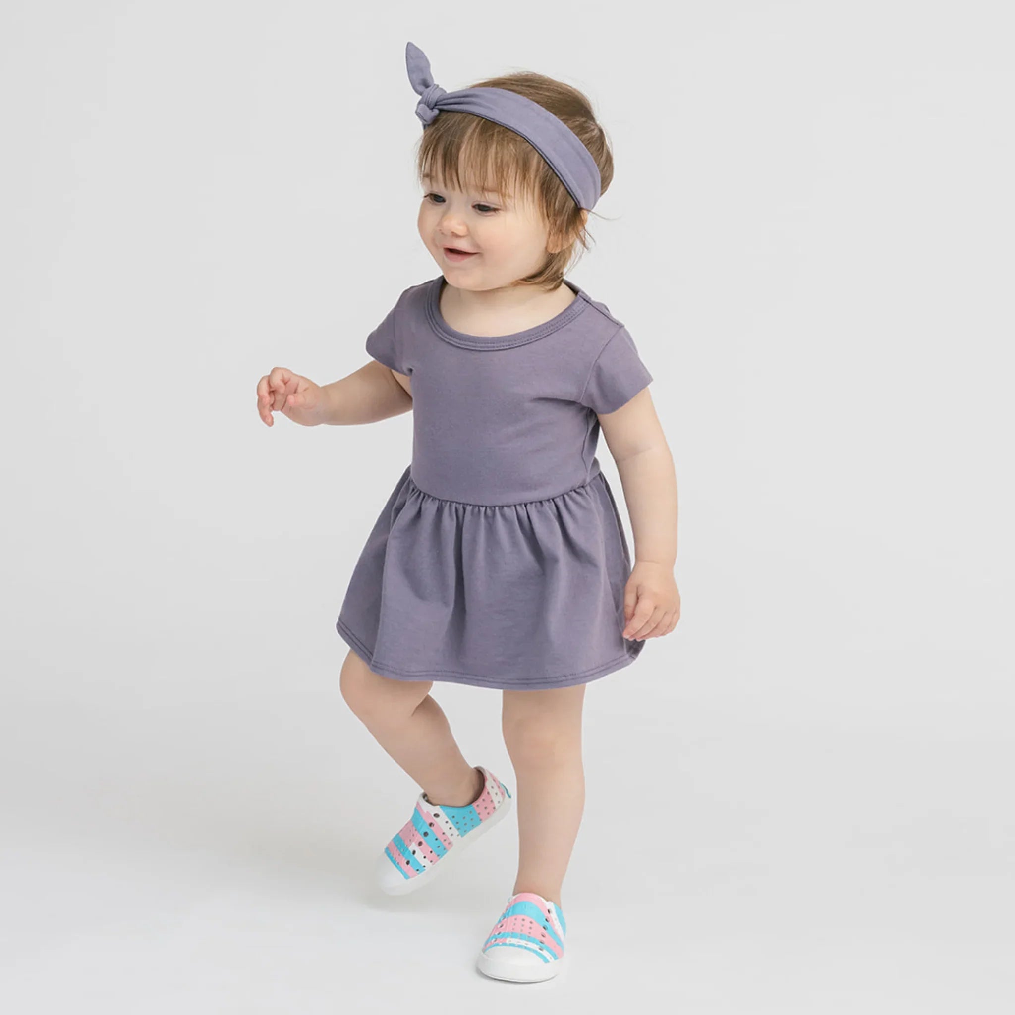 Bébé fille portant une robe vintage prune et un bandeau assorti, chaussures colorées
