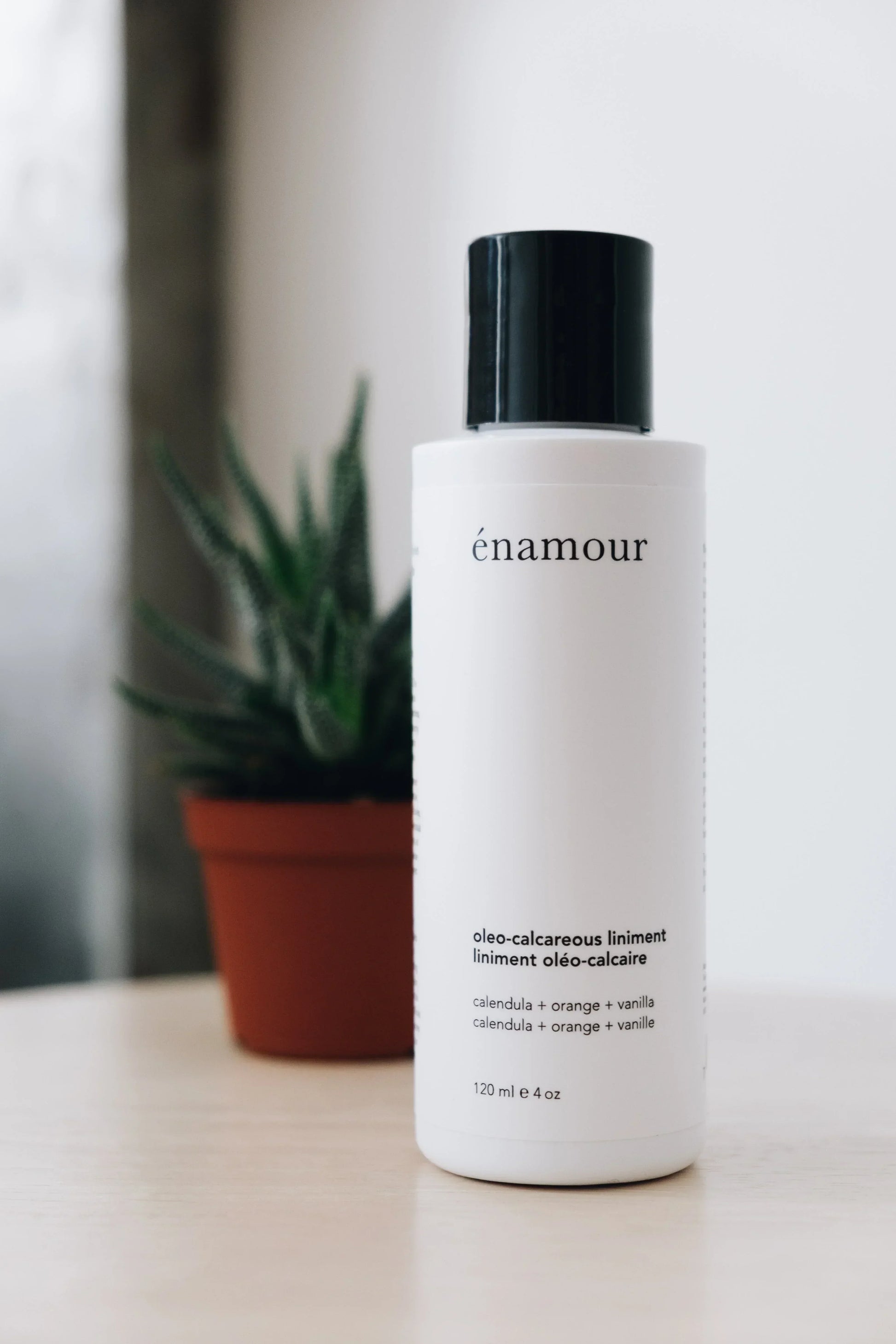 Flacon blanc de liniment oléo-calcaire Énamour avec un pot de plante verte en arrière-plan