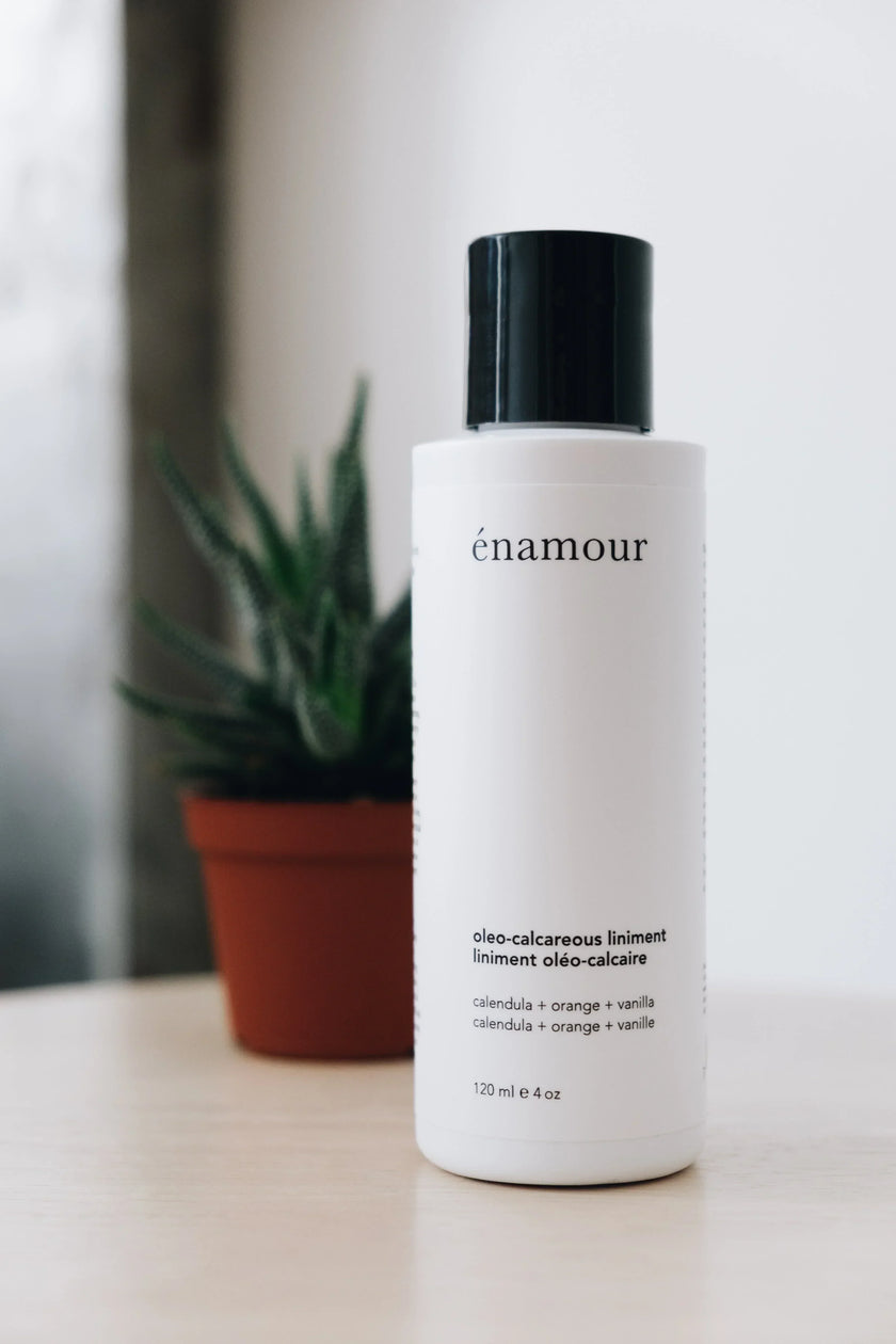 Flacon blanc de liniment oléo-calcaire Énamour avec un pot de plante verte en arrière-plan