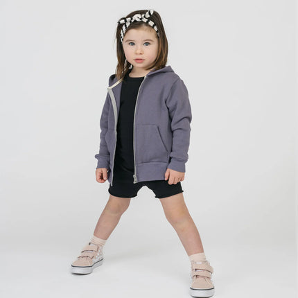Jeune fille debout en sweat à capuche violet, short noir, bandeau rayé noir et blanc, baskets beige